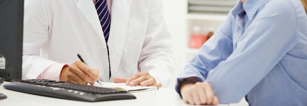 médico e paciente sentados em frente a um computador, médico passando detalhes para paciente