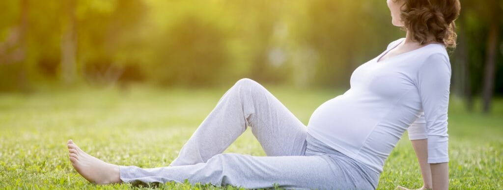 Mulher gestante sentada na grama, olhando para o horizonte